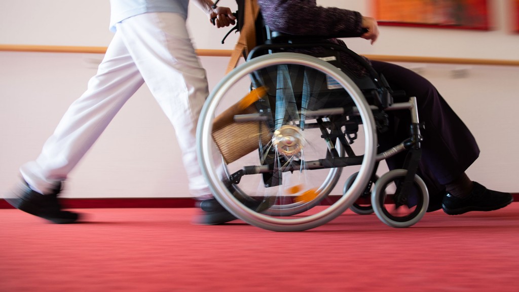 Ein Pfleger schiebt eine Bewohnerin im Rollstuhl über den Flur eines Pflegeheims (Foto: picture alliance/dpa/Tom Weller)