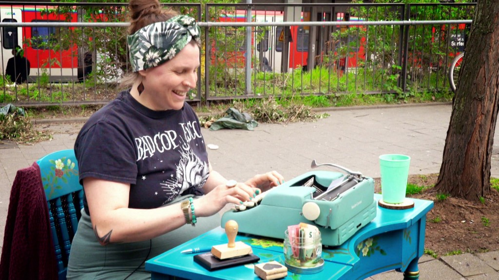Eine Frau sitzt draußen an einem Schreibtisch und tippt an einer Schreibmaschine