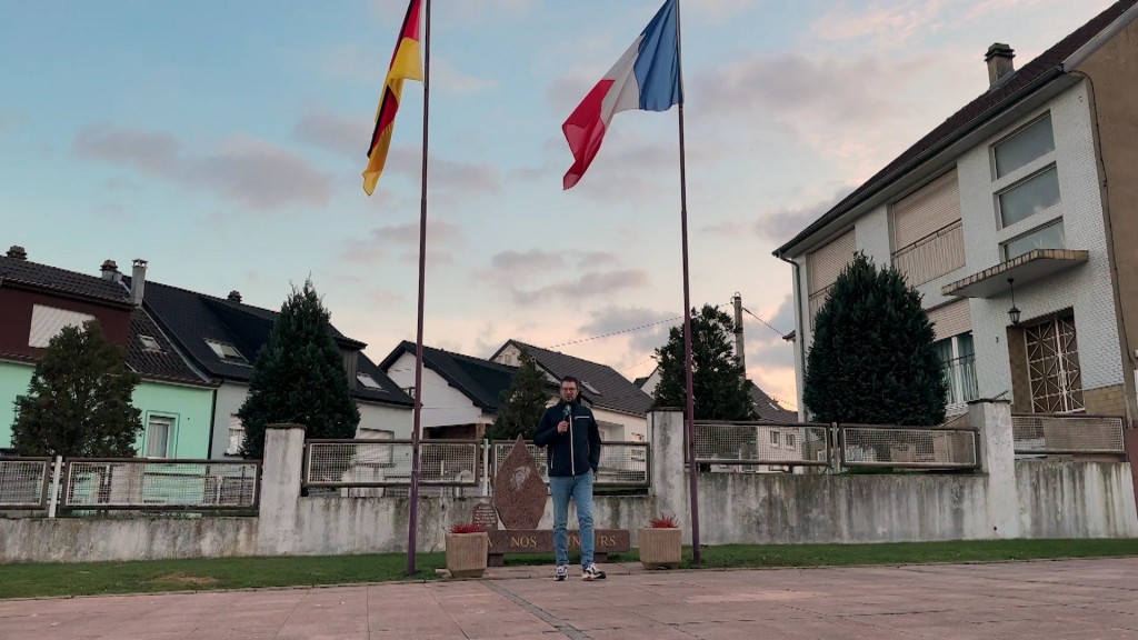 Foto: SR-Reporter Jonas Degen vor einer deutschen und französischen Flagge