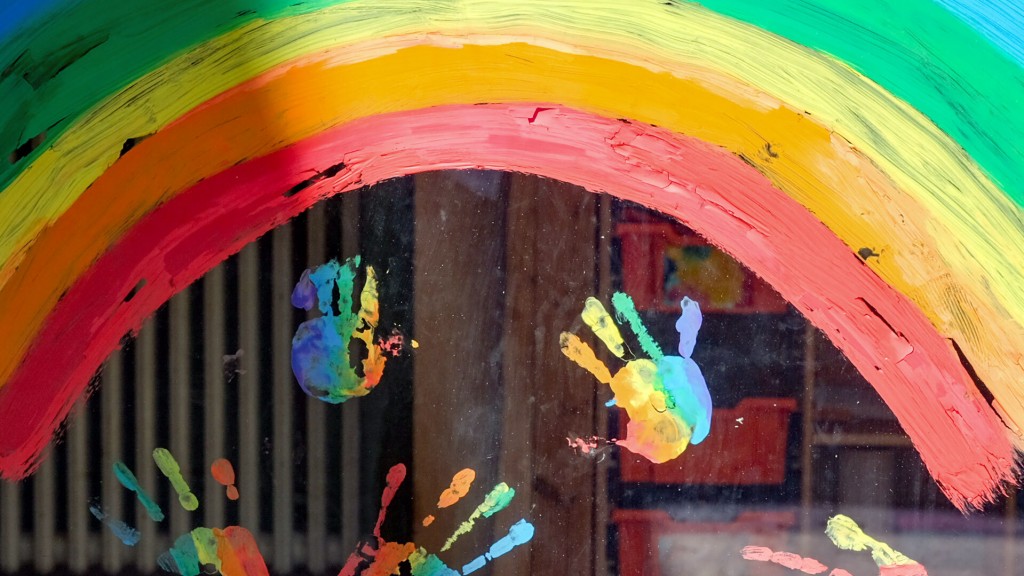Illustration: Bunte Kinder-Handabdrücke unter einem Regenbogen sind an einem Fenster zu sehen