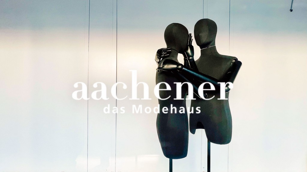 Zwei Schaufensterpuppen stehen trauernd hinter dem Logo des „Aachener“ Modehauses