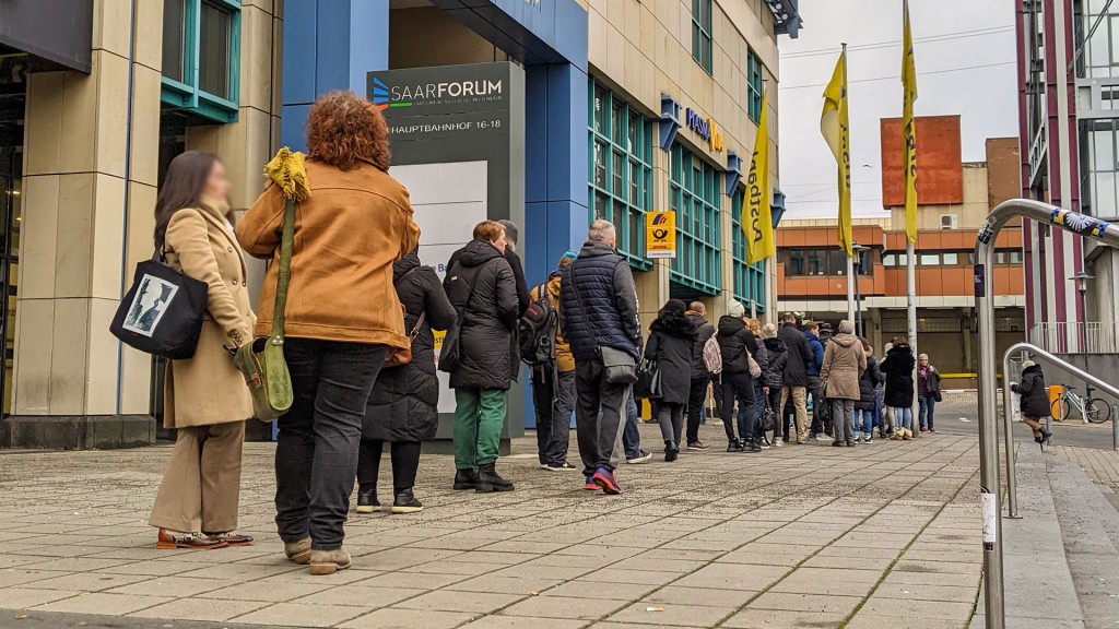 Zahlreiche Menschen stehen in einer Schlange vor der Poststelle neben dem Saarbrücker Hauptbahnhof an