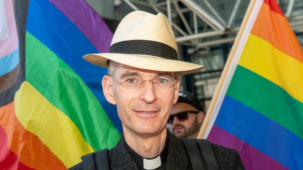Foto: Der katholische Priester Wolfgang Rothe vor zwei Regenbogenflaggen.