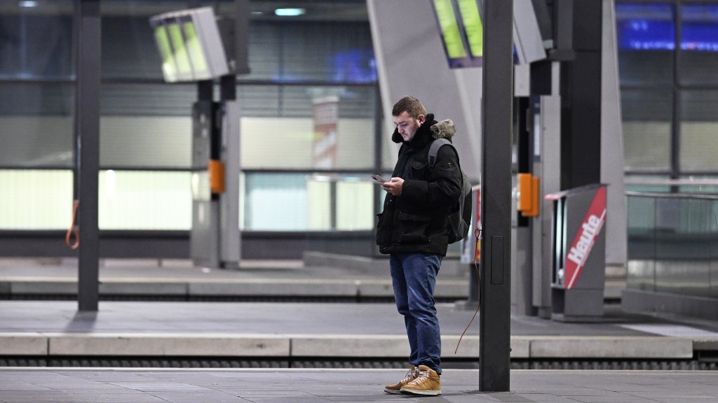 Ein Mann blickt auf sein Smartphone an einem leeren Bahnsteig.