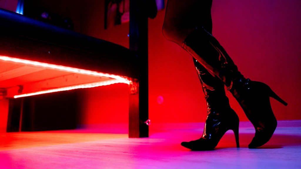 Symbolbild: Eine Prostituierte mit Lackstiefeln steht vor einem Bett mit roter Unterbeleuchtung.