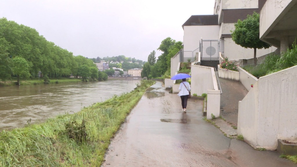 Eine Fußgängerin geht auf einem Gehweg neben der Saar mit einem Regenschirm