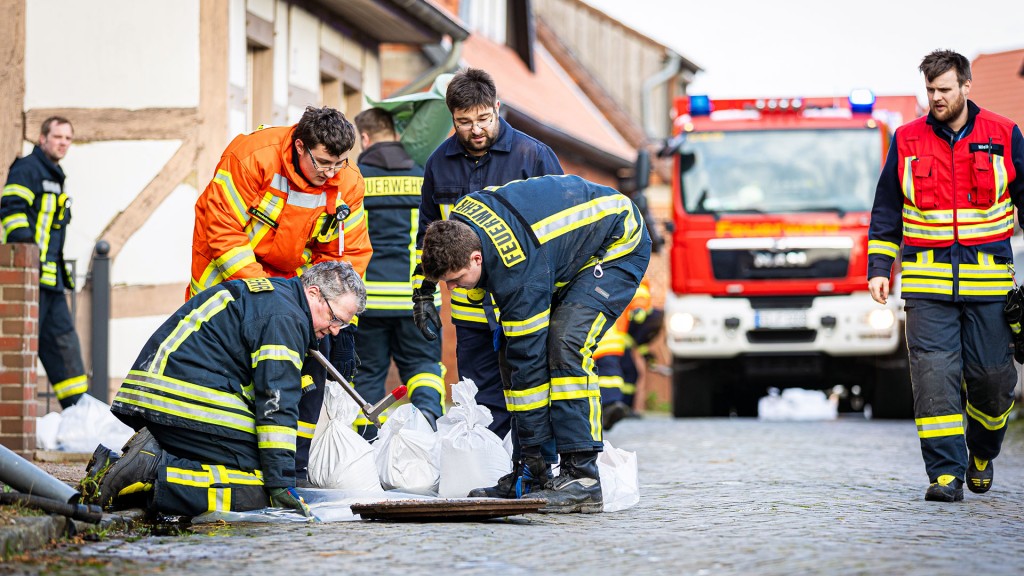 Foto: Einsatzkräfte der Feuerwehr mit Sandsäcken an einem Kanaldeckel