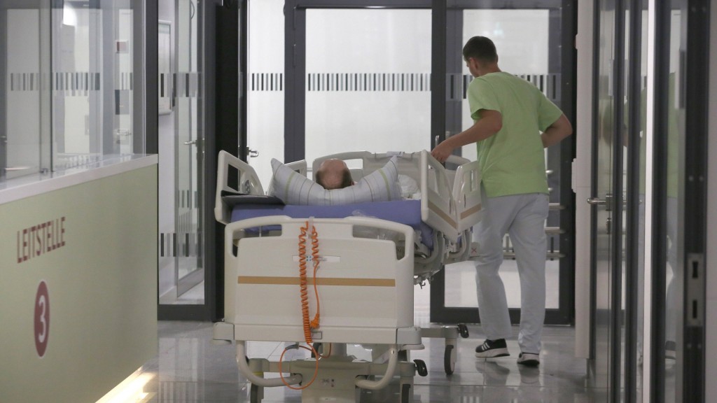 Ein Patient wird im Krankenbett von einem Pfleger über den Flur geschoben