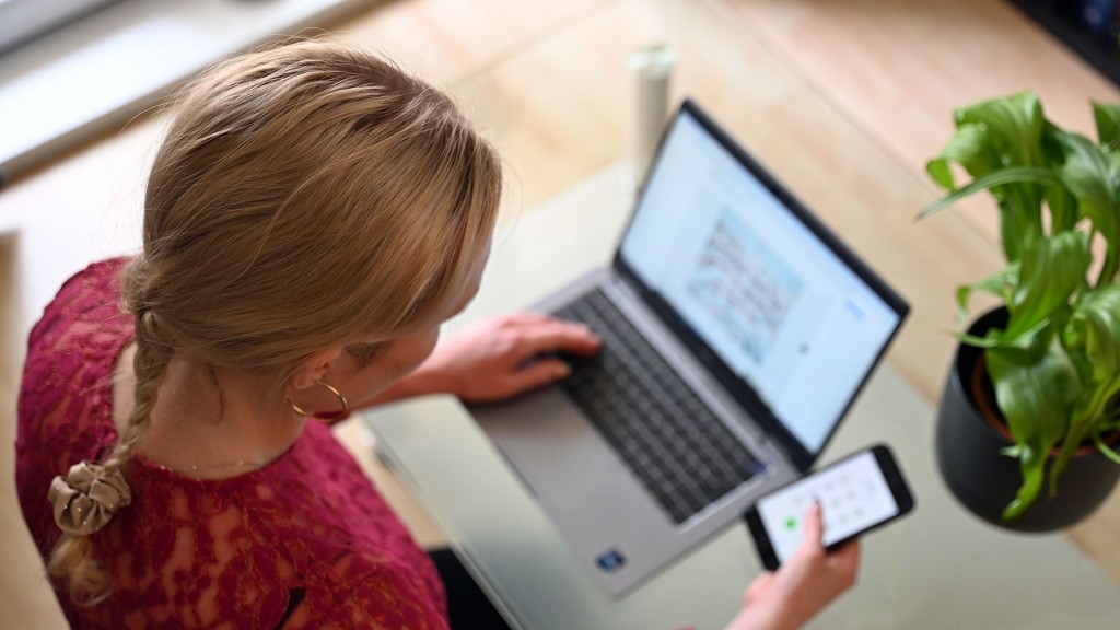 Eine Frau sitzt mit ihrem Smartphone vor einem Laptop