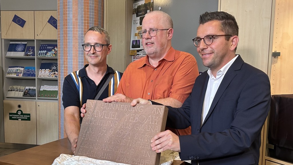 Vertreter der Aktion 3. Welt Saar und Oberbürgermeister Marc Speicher zeigen im Rathaus die Gedenktafel für Samuel Yeboah.