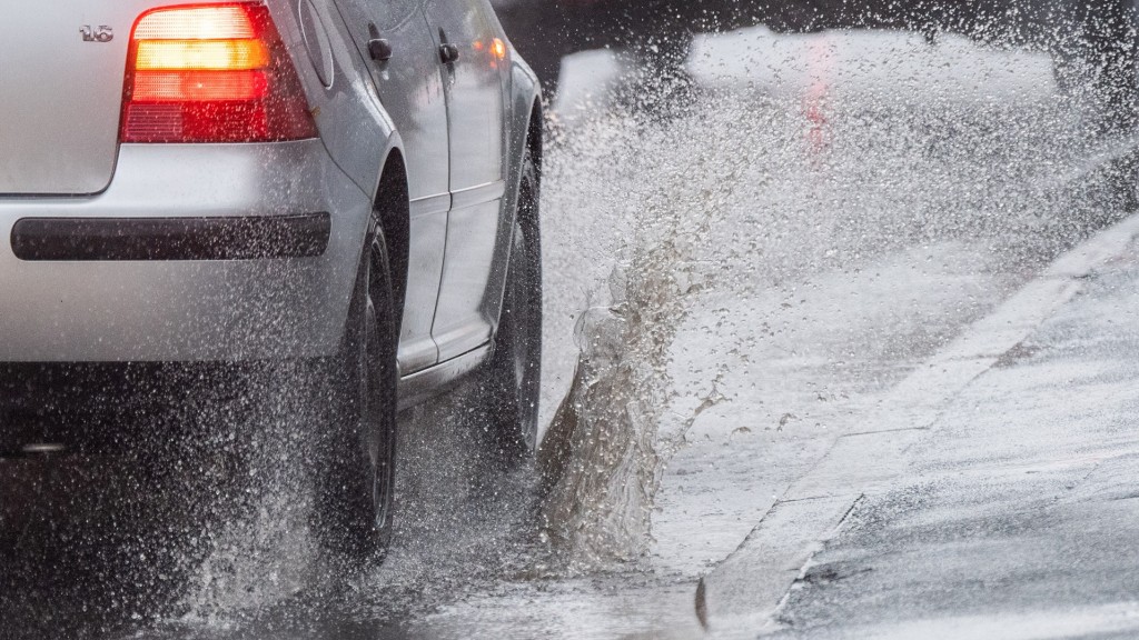 Foto: Ein Auto wirbelt Regenwasser auf, als es bei Dauerregen über eine Straße fährt.