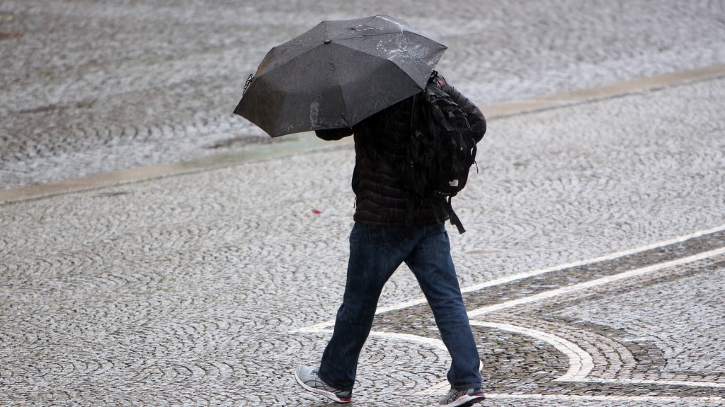 Foto: Mann mit Regenschirm überquert einen Platz während eines Regenschauers 