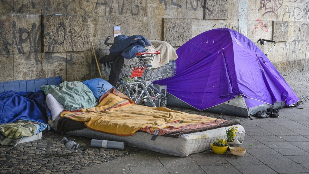 Schlafplatz eines Obdachlosen. Matratze auf dem Boden, Zelt und Einkaufswagen mit den persönlichen Gegenständen.
