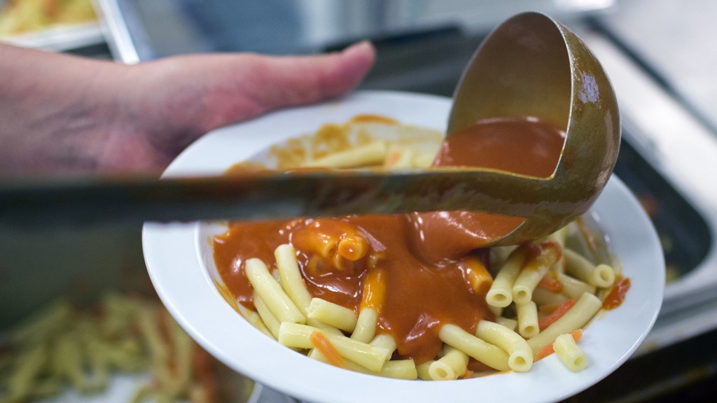 Mit einer Kelle wird das Essen auf Teller verteilt.
