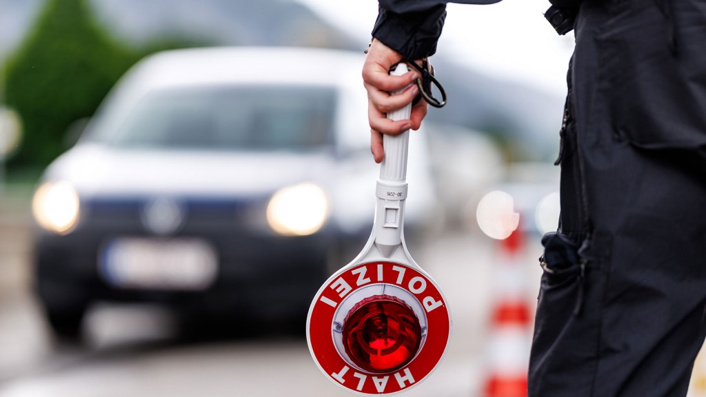 Ein Polizist hält eine Anhaltekelle in der Hand mit einem Auto im Hintergrund
