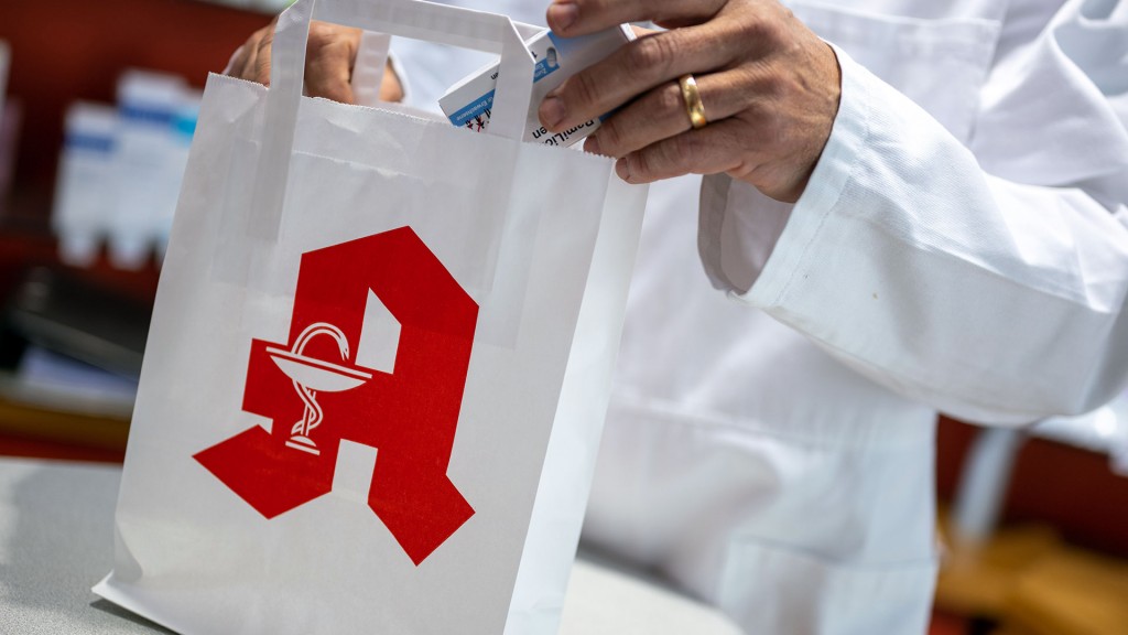 Foto: Ein Apotheker legt ein Medikament in eine Papiertasche mit Apotheken-Logo