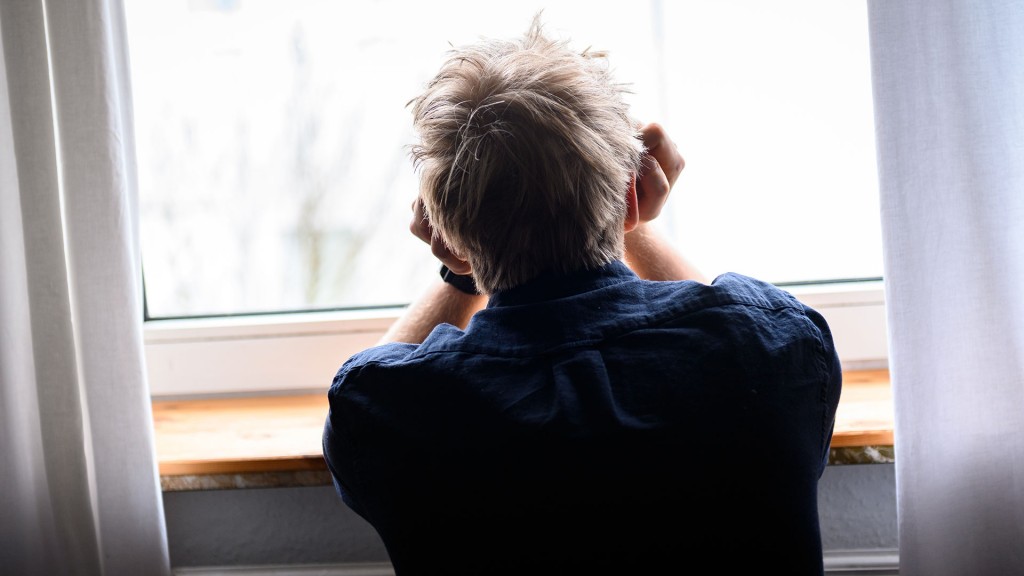 Eine Person sitzt mit dem Kopf in die Hände gestützt an einem Fenster