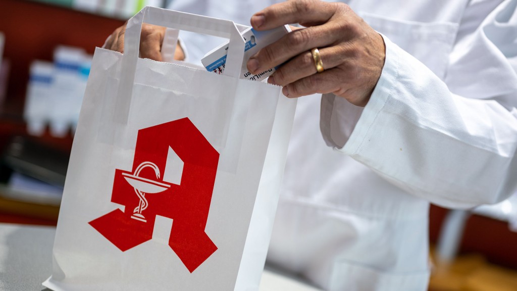 Ein Apotheker legt ein Medikament in eine Papiertasche mit Apotheken-Logo
