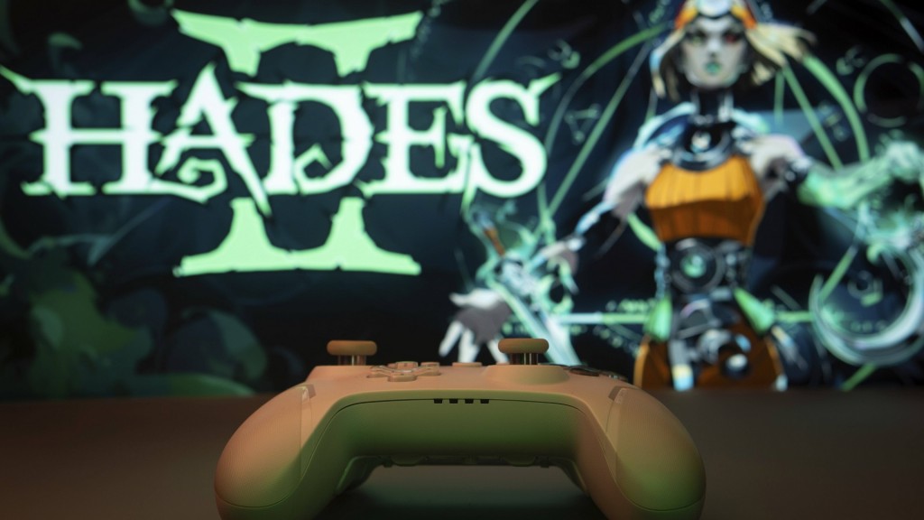 Nahaufnahme eines weißen Gamepads mit dem Hades II auf dem Bildschirm im Hintergrund 