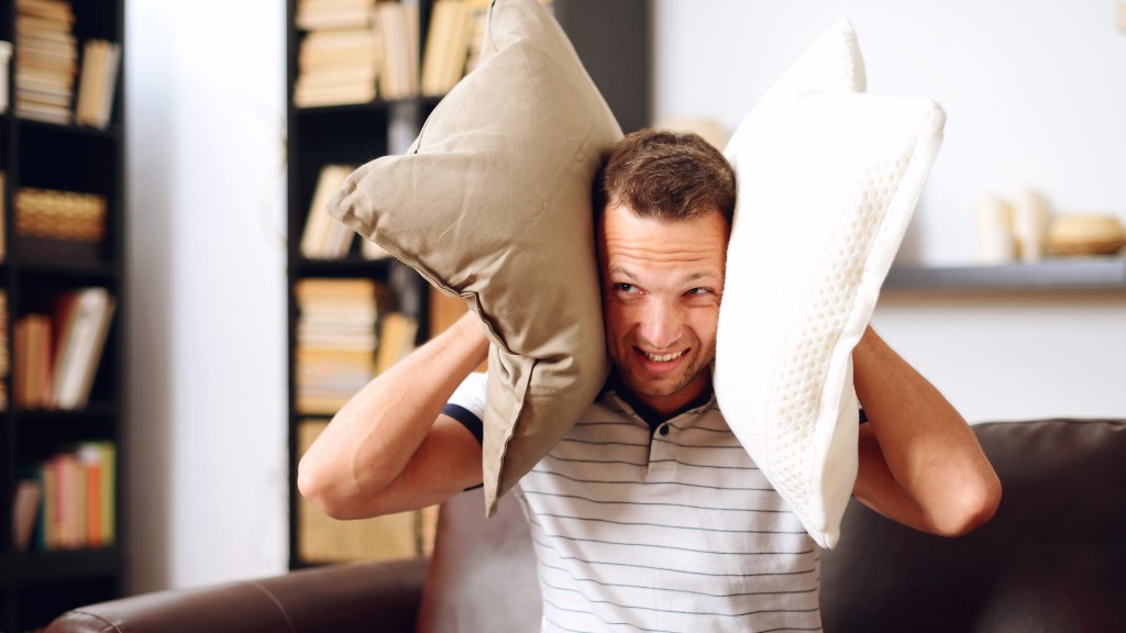Ein Mann hält sich mit zwei Kissen die Ohren zu