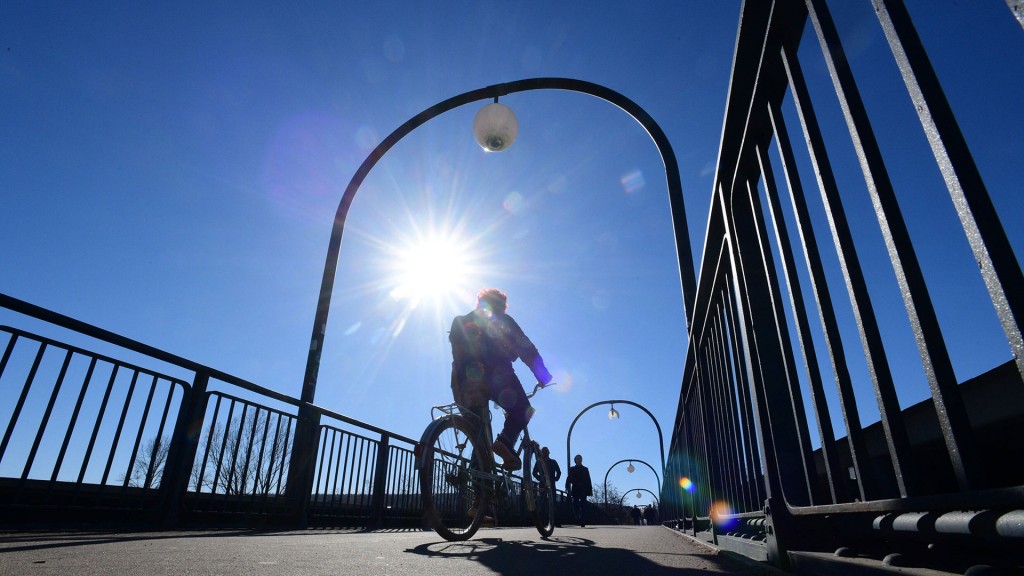 Fußgänger und ein Radfahrer überqueren bei warmem Wetter eine Brücke.