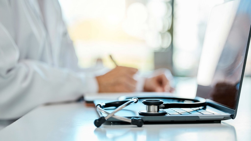 Ein Stethoskop liegt auf dem Computer eines Arztes im Hintergrund
