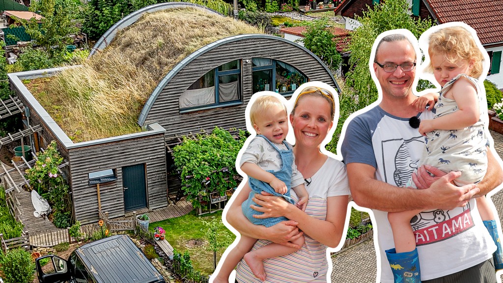 Foto: Eine junge Familie, die Eltern tragen jeweils ein Kleinkind auf dem Arm, steht vor ihrem Erdhügelhaus: Ein Holzhaus mit begrüntem Bogendach.