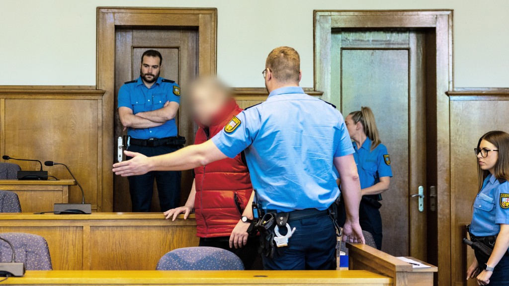 Der Angeklagte im Prozess um einen getöteten Gerichtsvollzieher wird von Justizvollzugsbeamten in den Saal 38 des Landgerichts Saarbrücken geführt. 