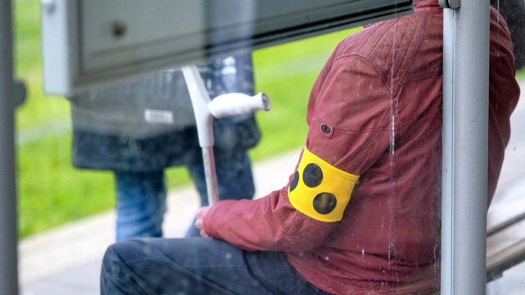 Foto: Eine Person sitzt an einer Bushaltestelle und wartet mit einer Armbinde für Sehbehinderten und eine Krücke im Hand