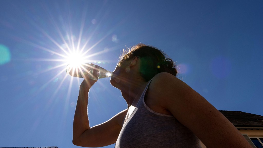 Eine Frau trinkt vor dem blauem Himmel mit der Sonne Wasser aus einer Flasche.