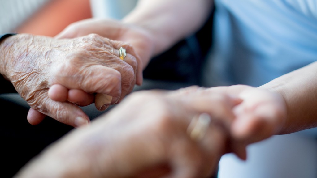 Eine Person hält die Hände einer kranken Seniorin.