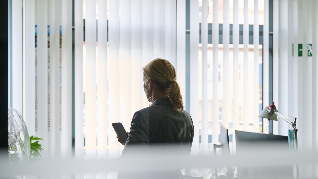 Foto: Eine Frau steht in einem Bürozimmer am Fenster und telefoniert