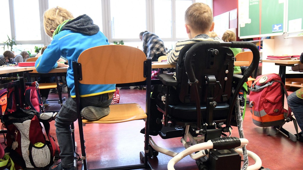 Foto: Kind mit Rollstuhl mit Mitschülern in einem Klassenraum