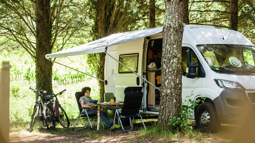 Ein Camper mit Markise und Campingmöbeln steht auf einem Stellplatz für Wohnmobile zwischen Bäumen