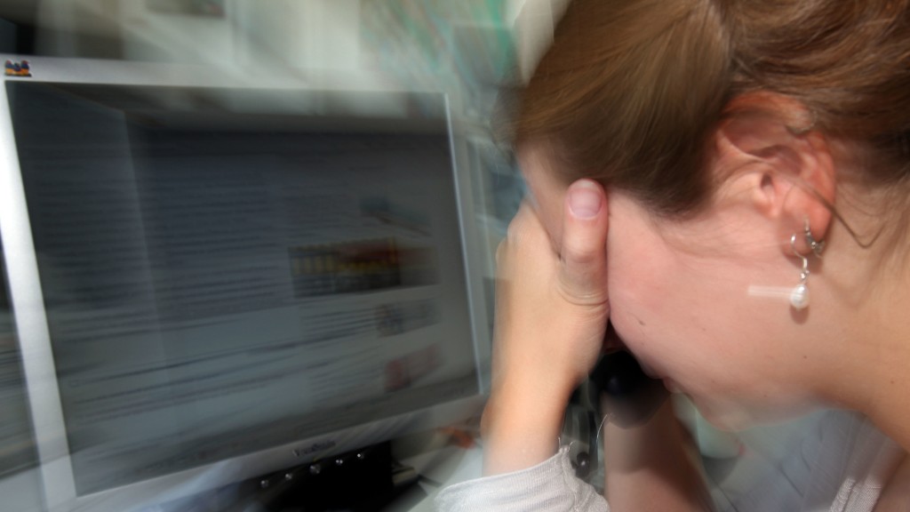 Frau vor Computerbildschirm, Kopf auf Hände gestützt