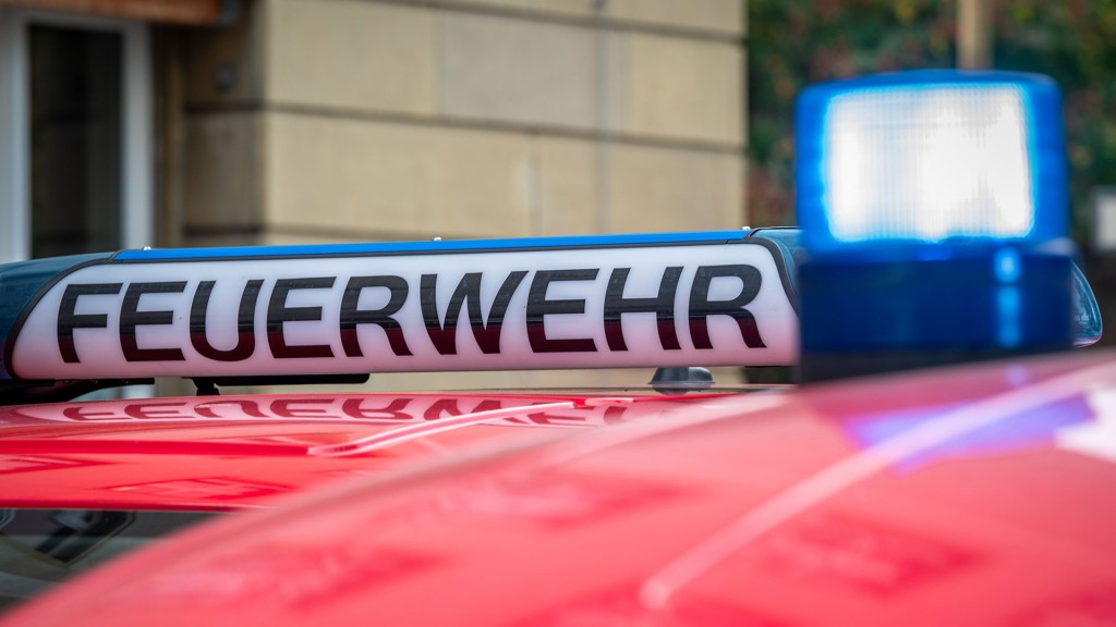 Foto: Der Schriftzug „Feuerwehr“ ist neben einem blau leuchtenden Sondersignal auf dem Dach eines Fahrzeuges der Feuerwehr zu sehen.