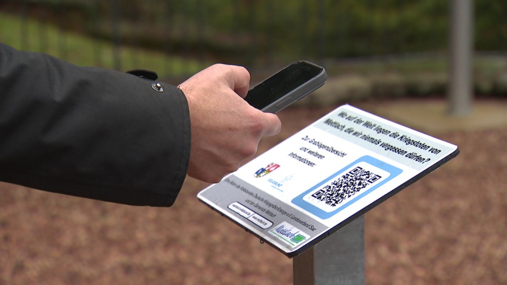 Foto: Eine Person scannt den QR-Code einer Informationsstele zur Erinnerung an Kriegstote