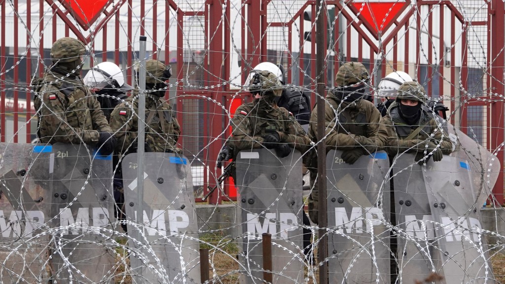 Polnische Sicherheitskräfte stehen hinter dem Grenzzaun am Grenzübergang Brusgi (Belarus) und Kuznica (Polen)  - Foto: picture alliance/dpa | Ulf Mauder