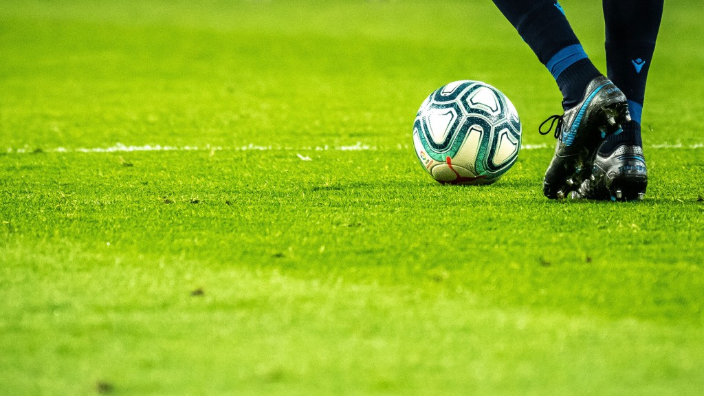 Foto: Nahaufnahme eines Fußballs und den Füßen eines Spielers auf dem Rasen