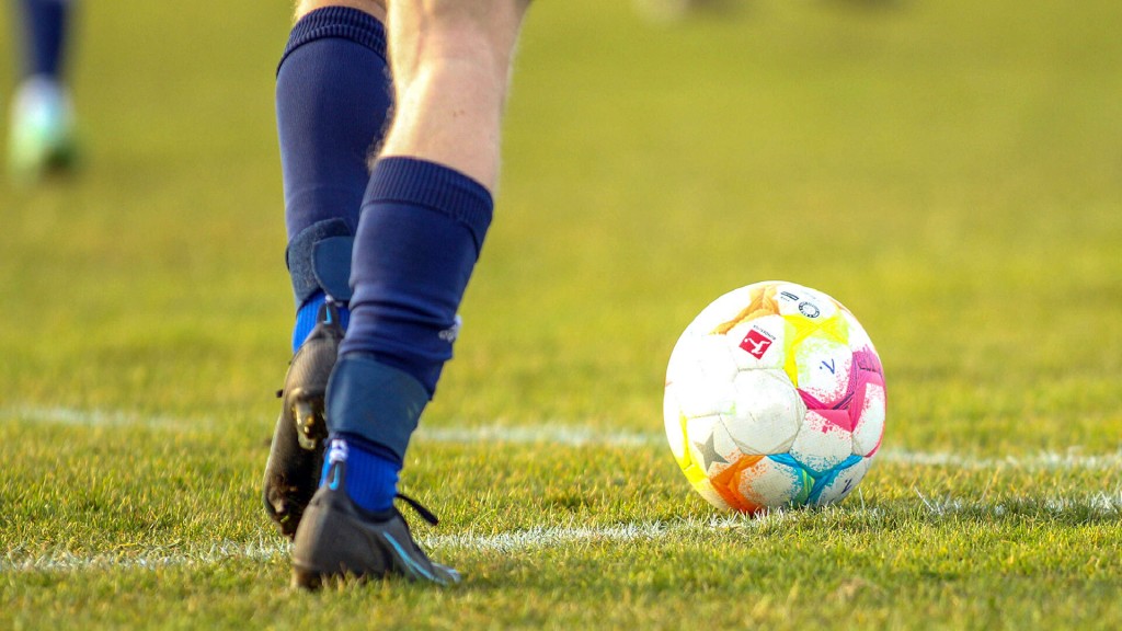 Symbolbild: Ein Fußball liegt vor Spieler-Füßen auf einem Rasenplatz