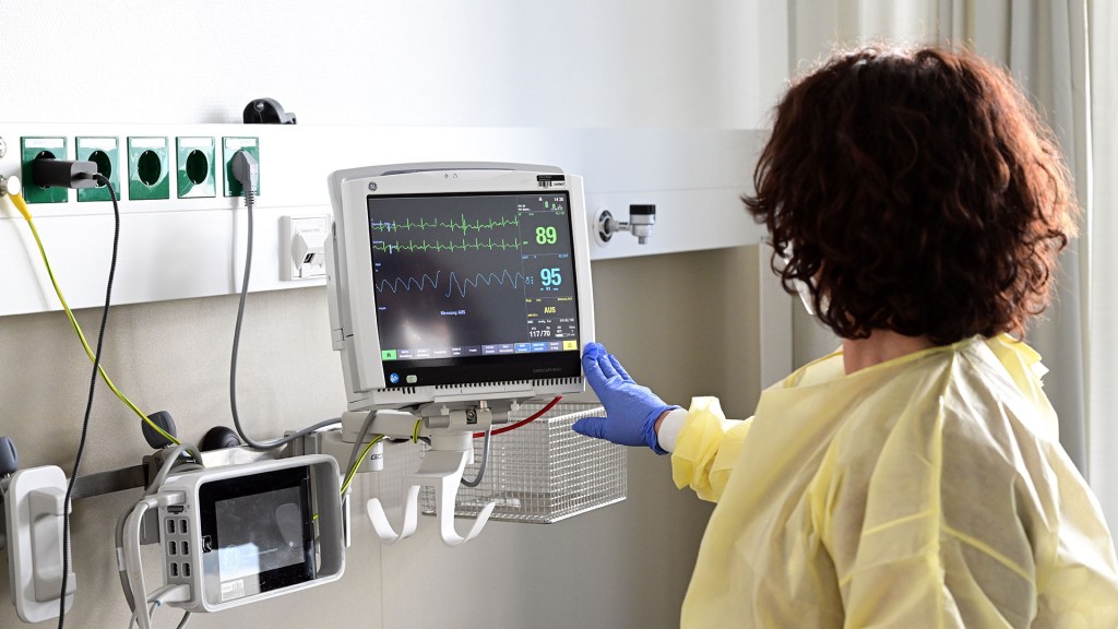 Foto: Eine Pflegerin schaut in einem Krankenzimmer auf einen Monitor einer Patientin