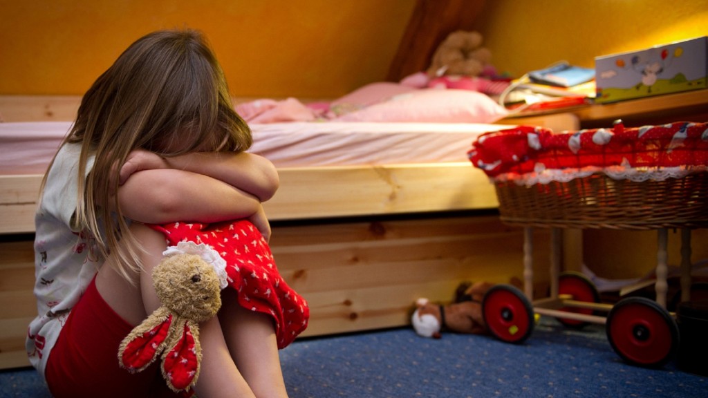 Ein kleines Mädchen sitzt weinend auf dem Fußboden in ihrem Zimmer.