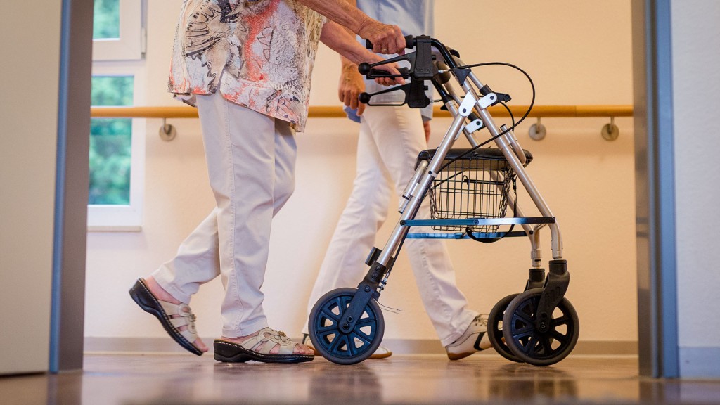 Eine Pflegekraft geht in einem Pflegeheim mit einer älteren Dame über einen Korridor