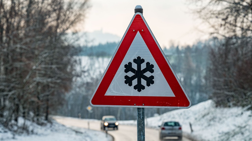 Ein Verkehrsschild mit einer Schneeflocke, das vor glatter Fahrbahn warnt steht am Straßenrand