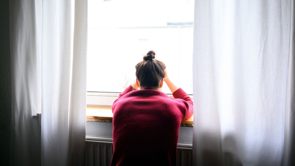 Foto: Frau steht vor einem Fenster und stützt ihren Kopfind die Hände 