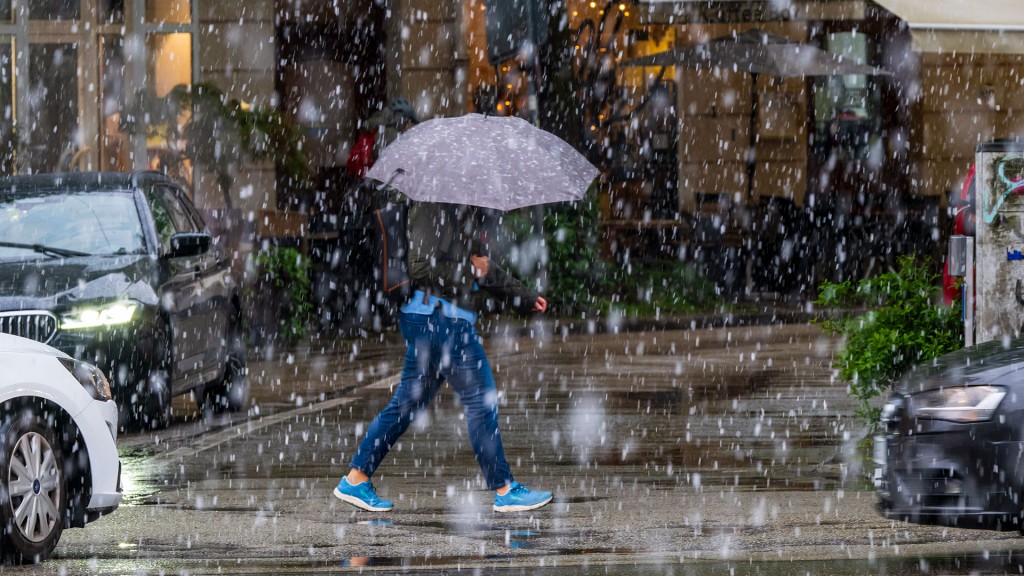 Eine Passantin mit Regenschirm geht bei heftigem Niederschlag über eine Straße
