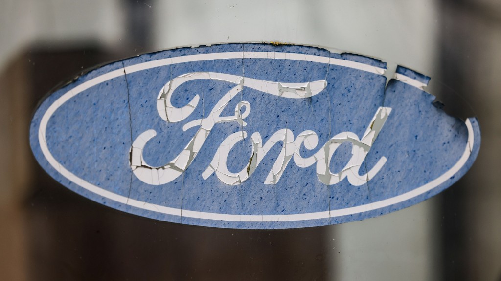 Foto: Ein abgeblättertes Logo von Ford hängt an einer Scheibe vor dem Werksgelände.