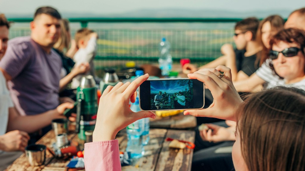 Eine junge Frau fotografiert eine Gruppe Reisende am Tisch mit einem Smartphone