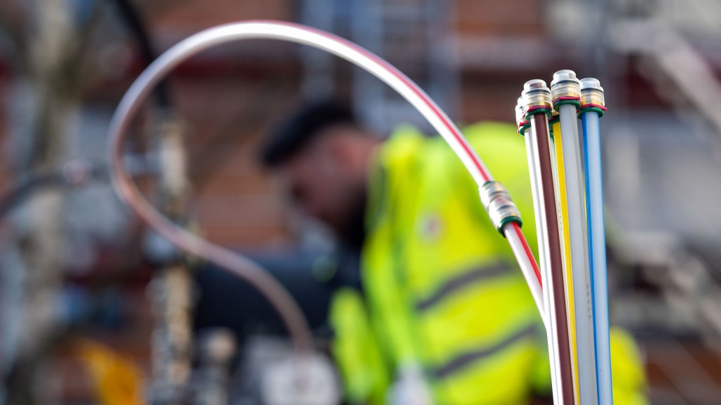 Foto: Ein Bauarbeiter steht hinter Leerrohren für Glasfaserkabel, die aus der Erde ragen