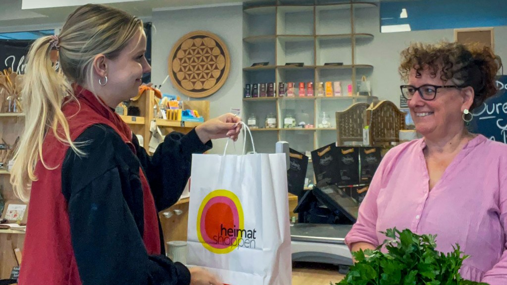 Eine Einkaufstüte mit dem Logo der Aktion „Heimat shoppen“ wird über eine Ladentheke gereicht